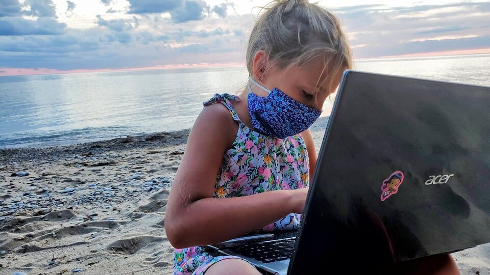 Une enfant sur la plage avec un ordinateur portable. 