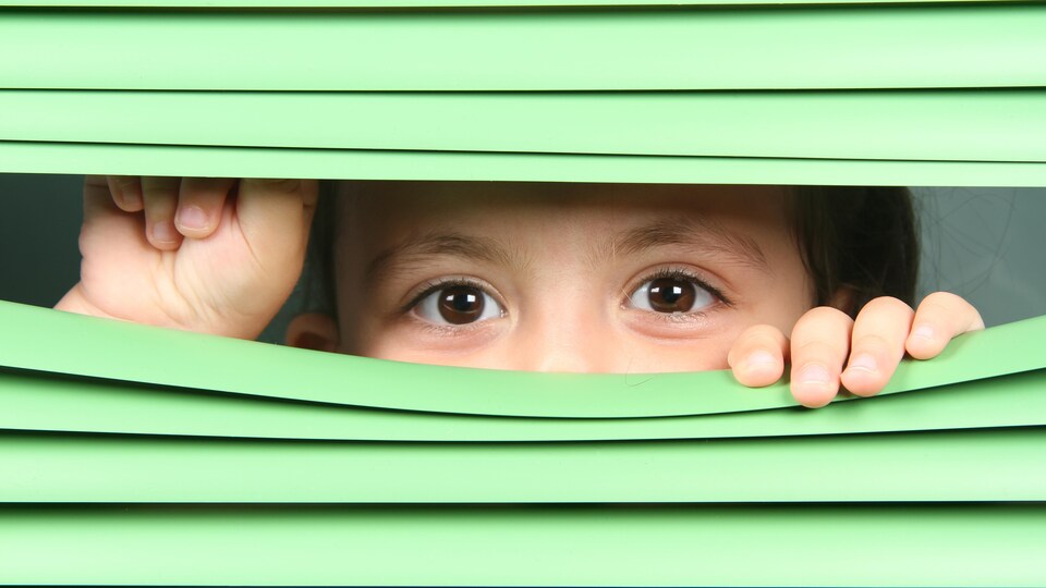 Un enfant regarde entre les lattes d'un store.