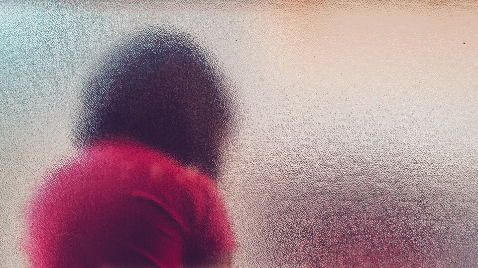Une silhouette d'une jeune fille, vue à travers une vitre givrée.