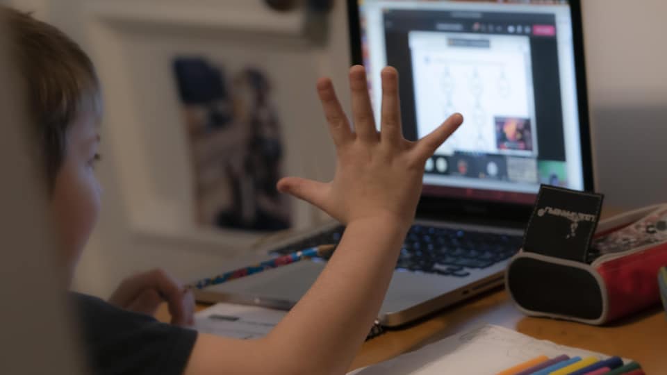 Un jeune garçon fait ses devoirs devant un écran d'ordinateur.