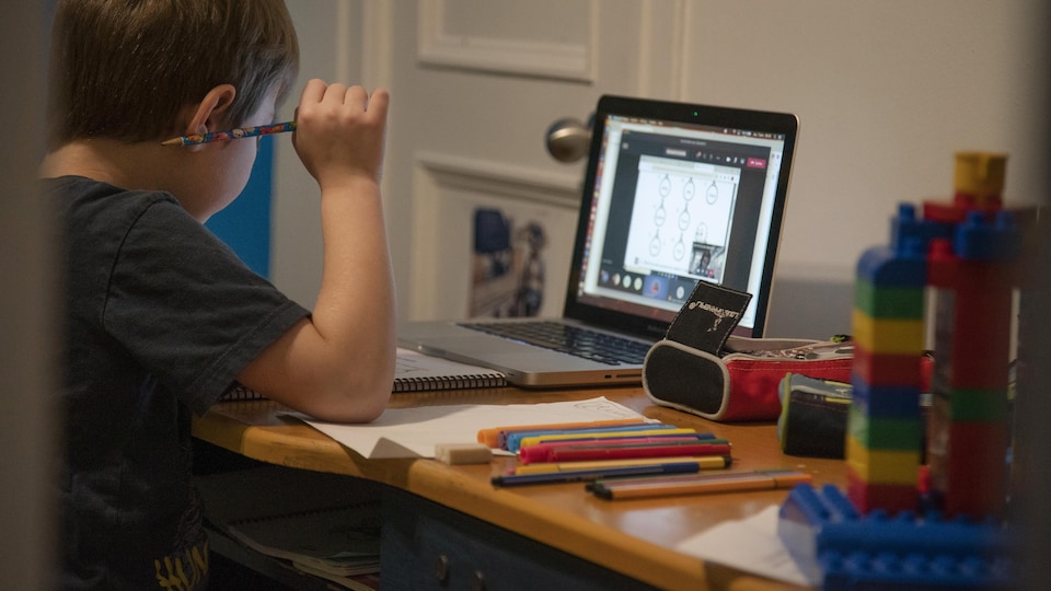 Un jeune garçon fait ses devoirs devant un écran d'ordinateur.