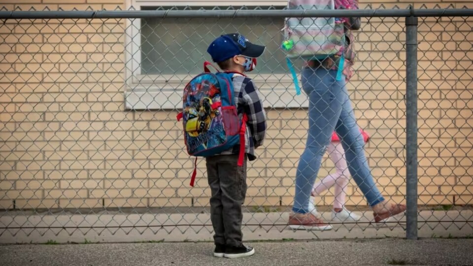 Un enfant seul, debout dans une cour d'école avec son sac sur le dos.