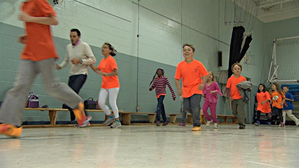 Students run in an elementary school gymnasium. 