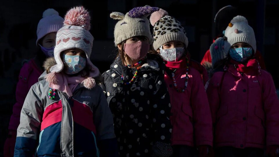 Des enfants chaudement habillés et masqués, dehors.