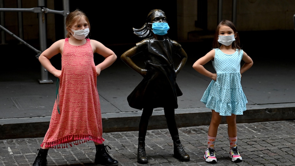 Deux fillettes portant des masques posent à côté de « La fillette sans peur » de Kristen Visbal, à New York.