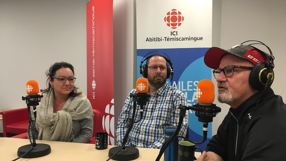 Trois personnes sont assises devant un micro autour d'une table.