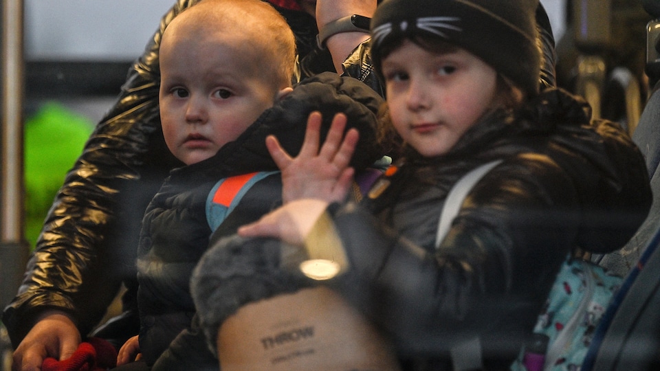 Deux enfants ukrainiens, dont l'un fait un salut de la main, sont aperçus à travers la vitre d'un autobus. 