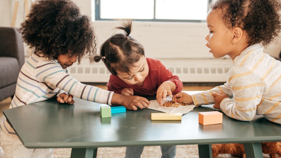 Trois fillettes jouent autour d'une table de salon.