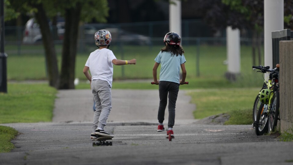 Deux enfants font de la trottinette et de la planche à roulette dans un parc.