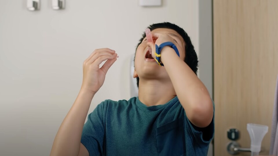 Arrêt sur image d'une vidéo explicative du nouveau test de dépistage gargarisant, où l'on voit un enfant vider un tube dans sa bouche.