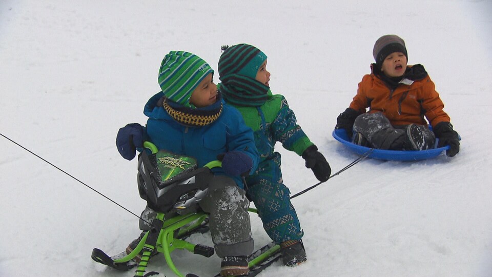 Trois enfants sur des traîneaux dans la neige.