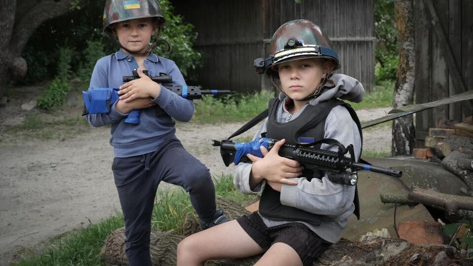 Deux jeunes garçons ukrainiens jouent aux soldats portant un casque et un fusil. 