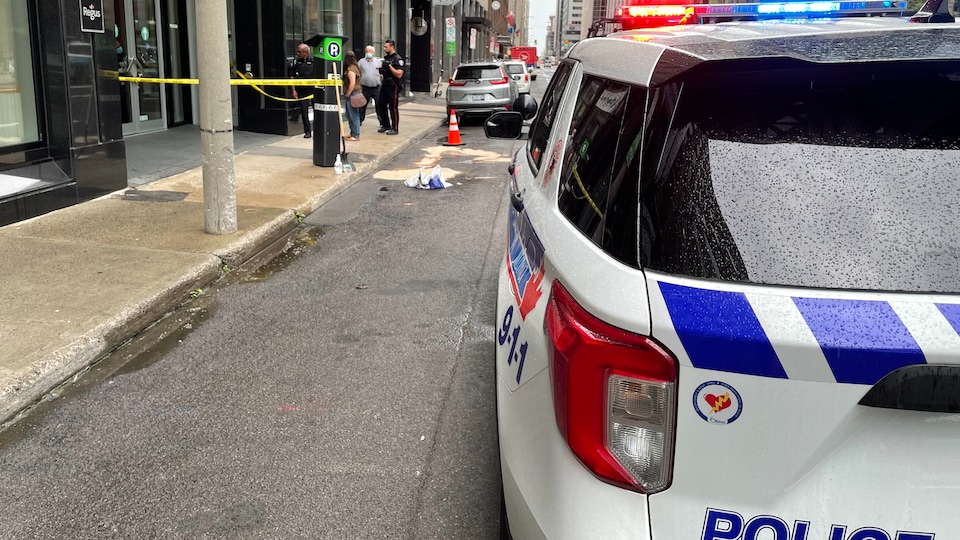 Un véhicule de police est stationné à proximité d'immeubles. Un cordon barre l'entrée d'un immeuble.