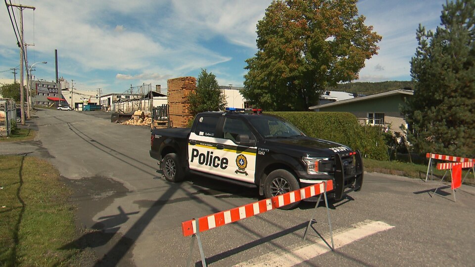 Une camionnette de la Sûreté du Québec est stationnée à proximité d'une usine endommagée par un incendie.