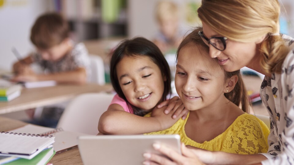 Une enseignante montre quelque chose à deux élèves sur une tablette.