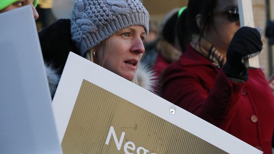 Une manifestante l'air triste, tenant une pancarte.