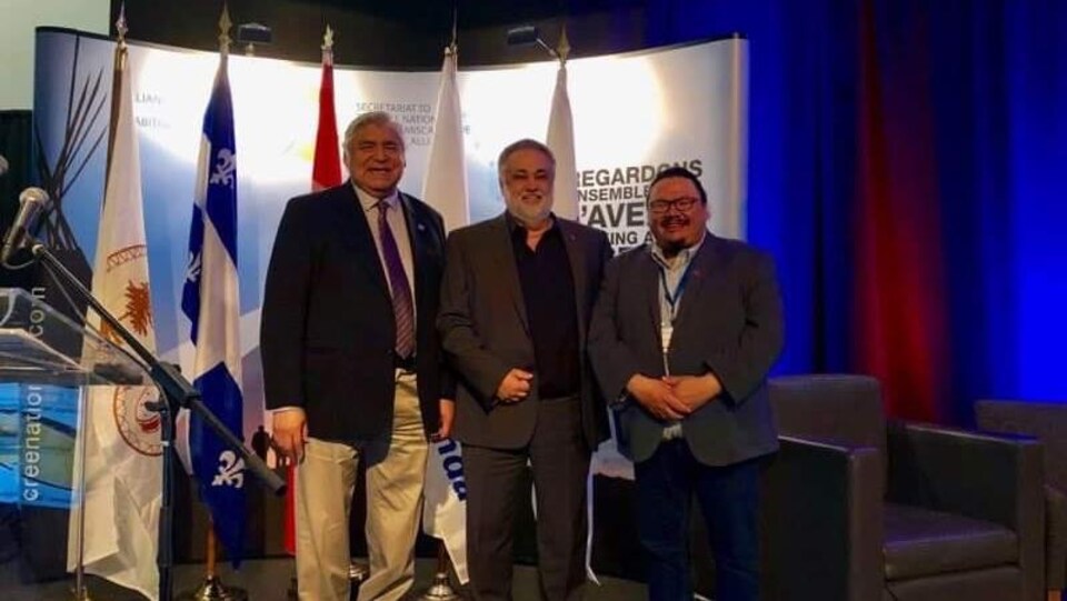 Trois hommes posent côte à côté lors d'un événement.