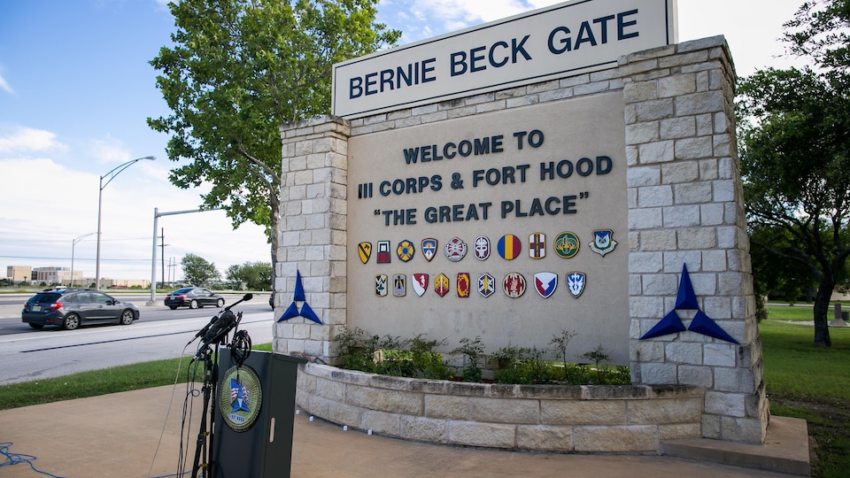 L'une des entrées du Fort Hood, où il est écrit «Bienvenue au 3ᵉ corps des États-Unis et à Fort Hood» et devant laquelle on voit un micro et des automobiles qui circulent dans la rue.