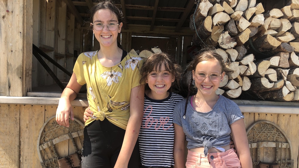 Les trois sœurs posent devant un étalage de bûches de bois. 