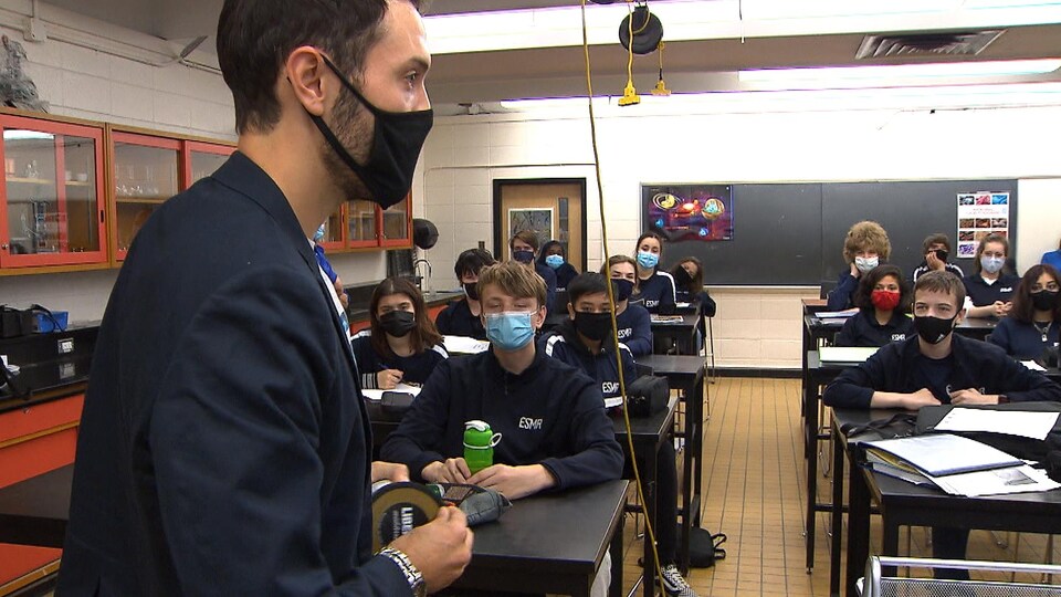 Daniel Jacob, debout devant la classe et portant un masque, s'adresse aux élèves assis devant lui.