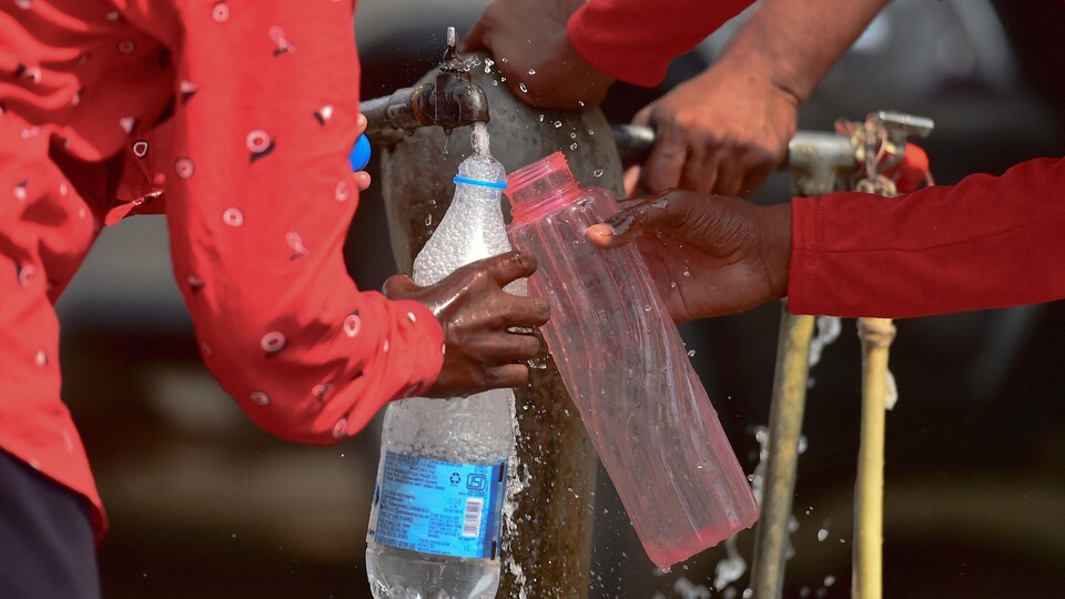 Des hommes remplissant des bouteilles d'eau à partir d'un robinet dans une rue d'Allahabad, en Inde.