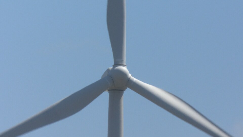Un gros plan sur une éolienne, dans un ciel bleu.