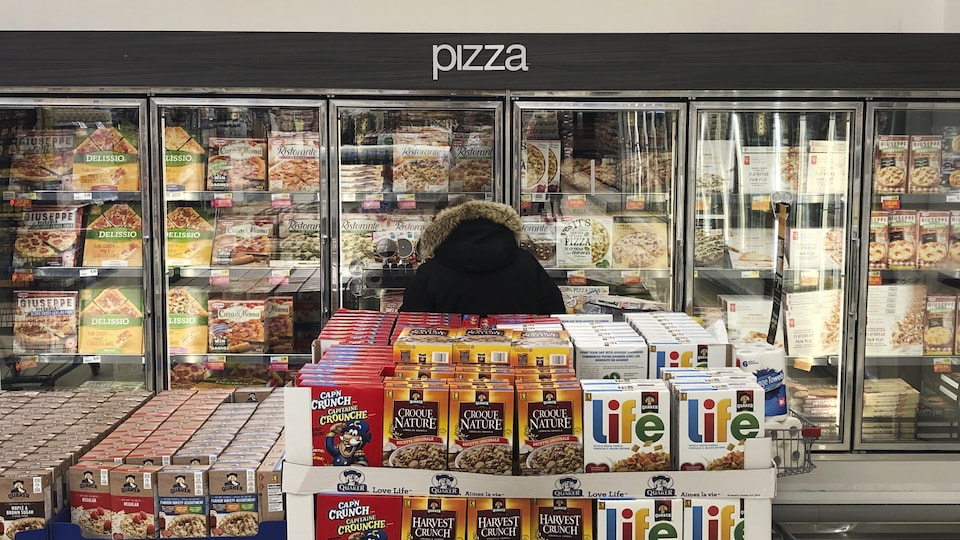 Un homme se trouve dans le rayon des pizzas surgelées dans une épicerie.
