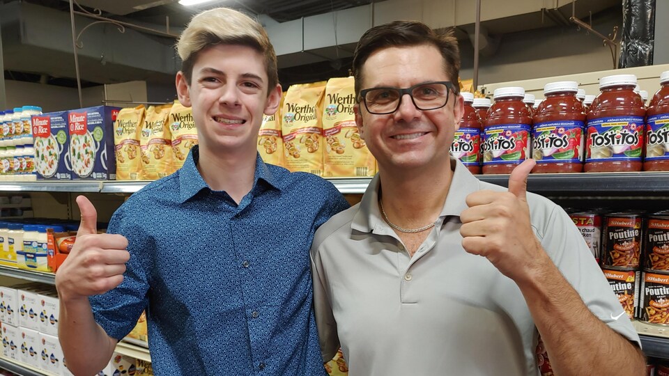 Les propriétaires, Charles-William Delisle et son père Jean-François Delisle, bras dessus, bras dessous devant une étagère d'épicerie.
