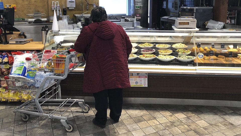 Une femme accoté sur son chariot devant un comptoir dans un magasin d'alimentation.