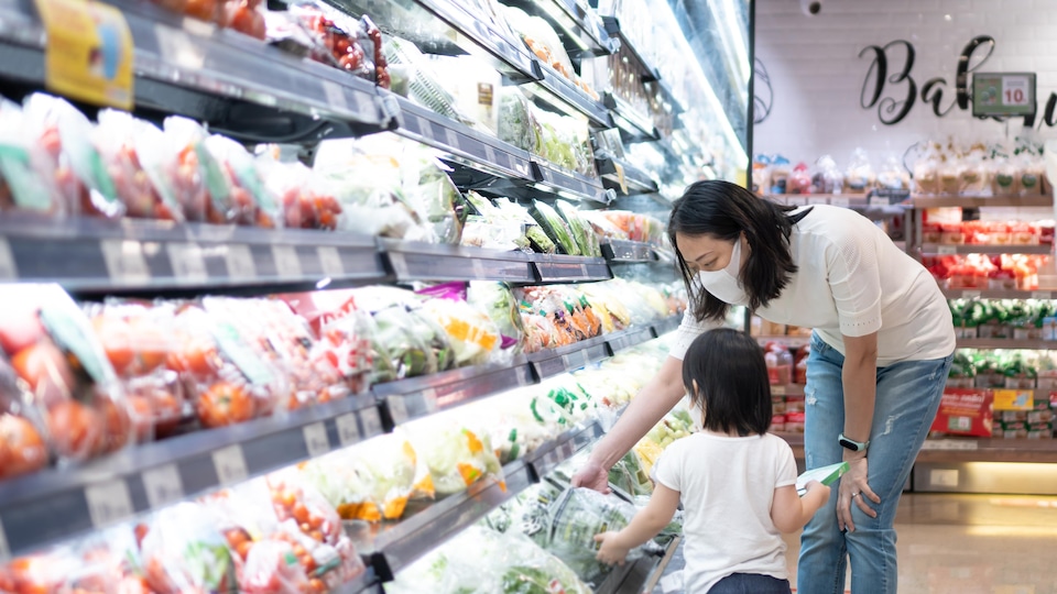 L'allée des légumes réfrigérés au supermarché; une mère et son enfant choisissent une laitue.