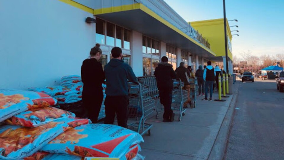 Des clients attendent en ligne avec leur panier à l'extérieur d'un supermarché.