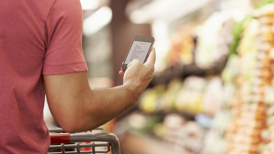 Un homme consulte sa liste d'épicerie sur son cellulaire alors qu'il marche dans un supermarché.