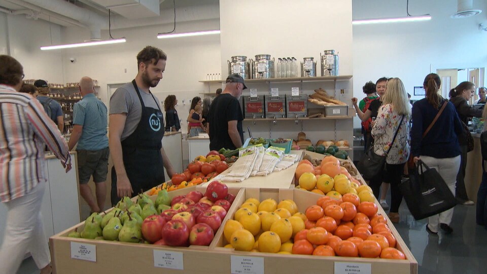 Des gens devant des étalages de fruits, de légumes et d'autres produits alimentaires.