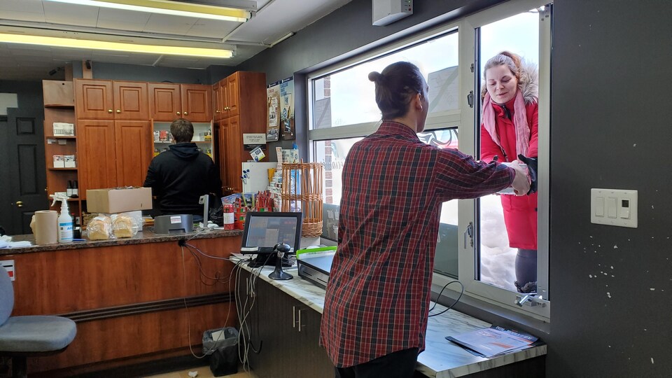 Un employé remet une boîte à une cliente à travers une petite fenêtre verticale.