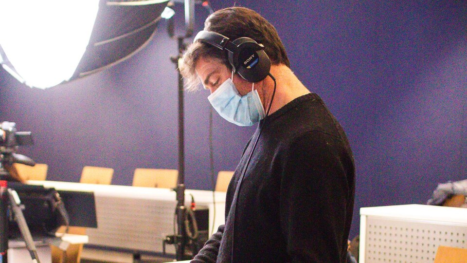 A man with headphones and wearing a face mask is manipulating sound recording equipment.
