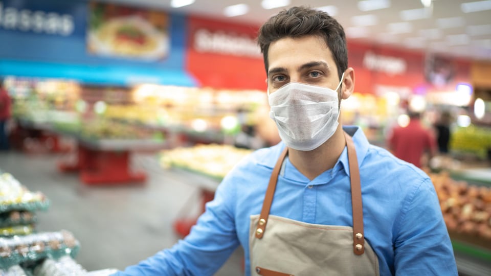 Un travailleur dans une épicerie porte un masque.