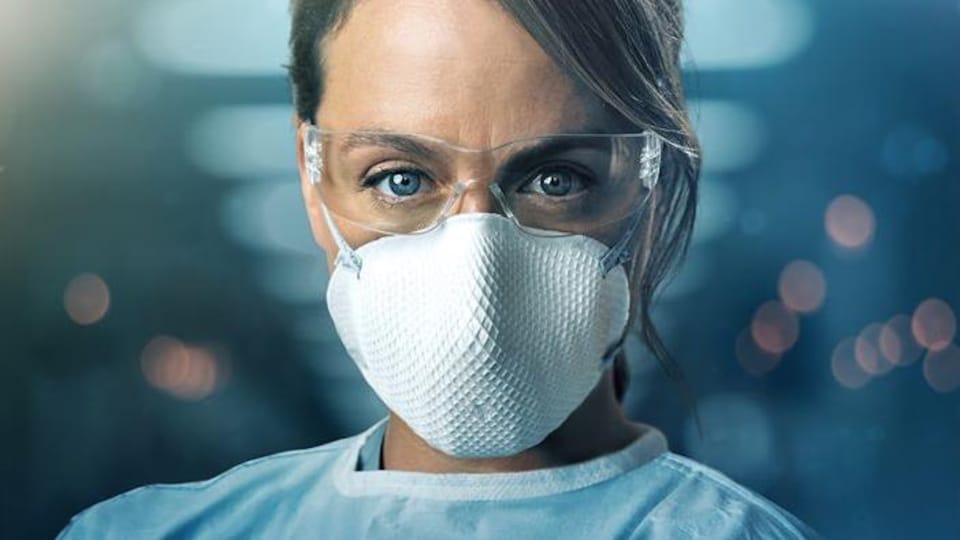 Une femme porte un sarrau, un masque et des lunettes de protection.