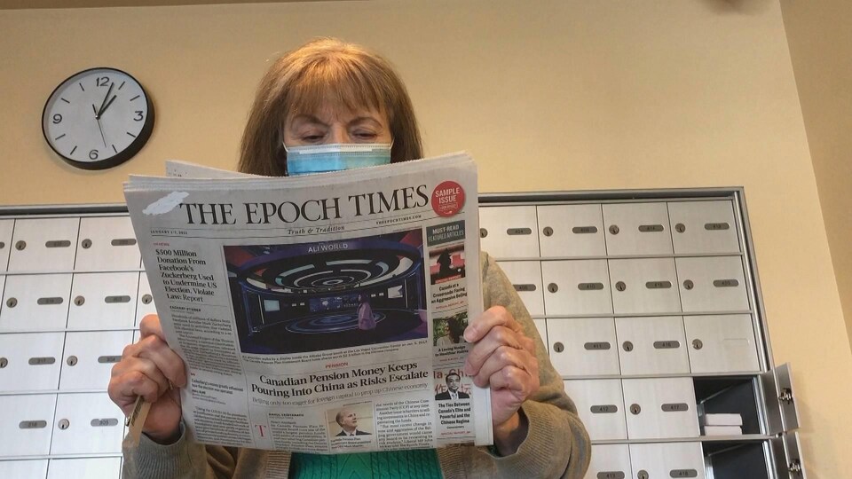 Une femme tient une copie du journal « The Epoch Times » devant une rangée de boîtes postales.