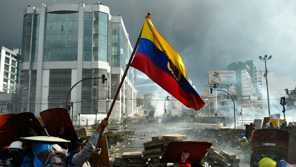 Des manifestants brandissent un drapeau équatorien, au milieu des gaz lacrymogène.