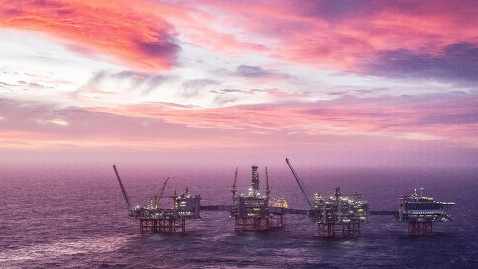 Des plateformes pétrolières en mer sous un ciel rose et mauve.