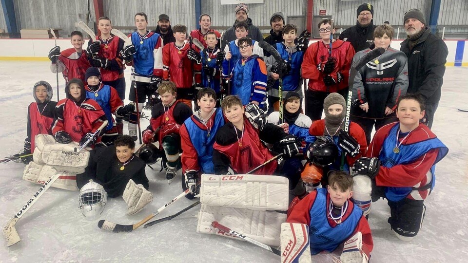 Un groupe de jeunes joueurs de hockey prend une pose d'équipe sur la glace en compagnie de quelques bénévoles.