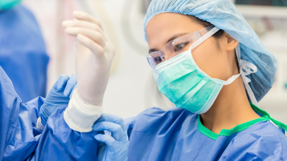 Une jeune infirmière aide un chirurgien à enfiler un gant en caoutchouc.