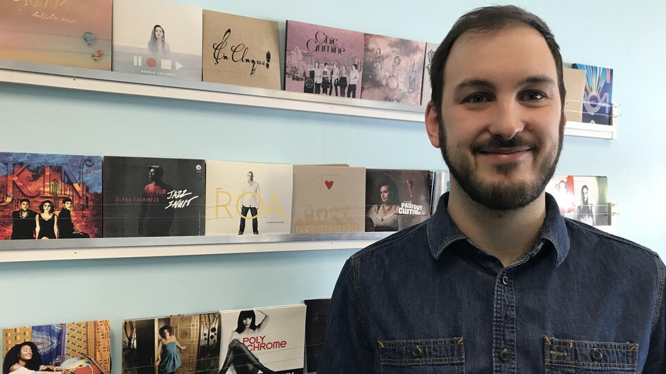 un homme qui sourit, avec derrière lui des présentoirs sur lesquels on voit des CD de musique.