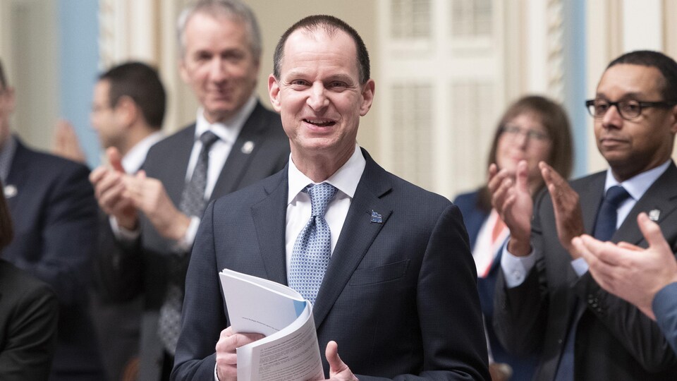 Le ministre tient le document du budget dans ses mains.