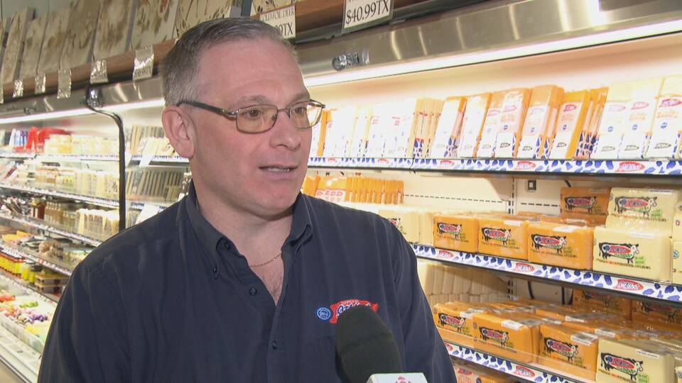 Un homme en entrevue devant un rayon de fromages. 