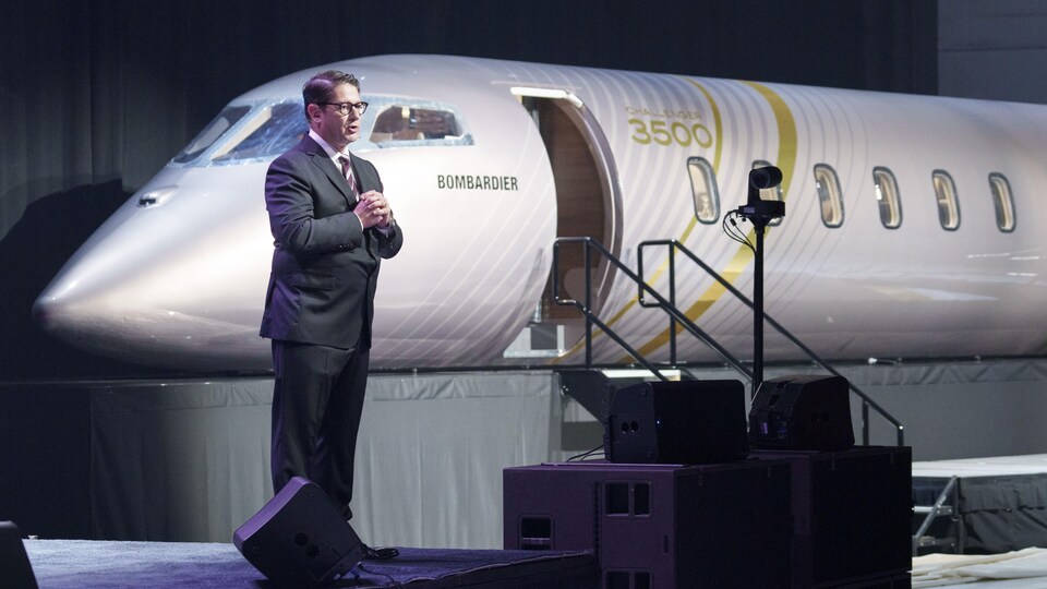 Éric Martel debout à côté d'un avion dans une salle décorée de rideaux.