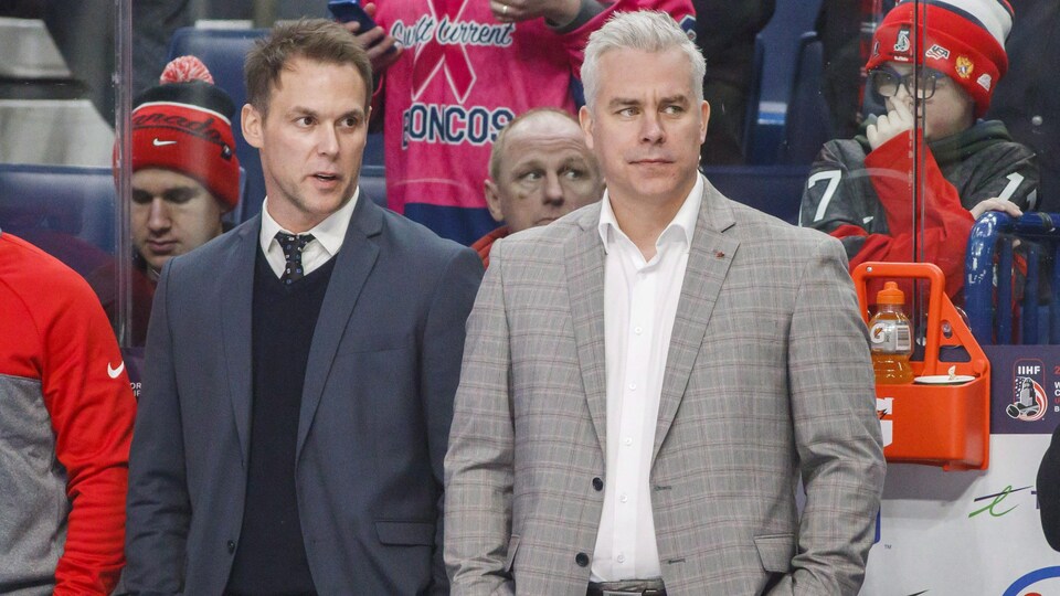 Éric Raymond et Dominique Ducharme sont debout derrière le banc.
