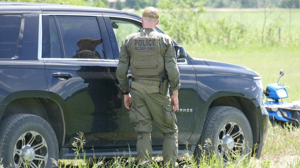 Un agent du de dos près d'un véhicule de police dans un milieu rural.