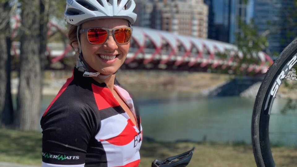 Erica Wiebe, casquée, tient son vélo du guidon des deux mains, et sourit.