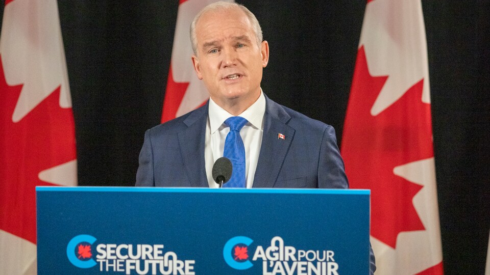Erin O'Toole prononce un discours derrière un podium avec derrière lui des drapeaux du Canada. 
